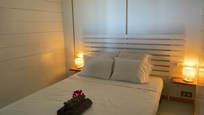 A neatly made bed with white linens, two bedside lamps, and a small table with a lamp. - Charming T1 50 m from Anse Bonneville beach, beach and idleness guaranteed! (La Trinité)