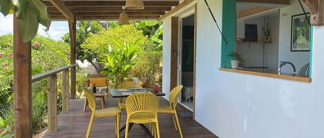 A wooden deck with yellow chairs and a table, a hanging light fixture, and a view of a lush garden.