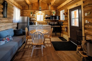 A log cabin interior with a kitchen, dining area, and a sofa with a decorative pillow.