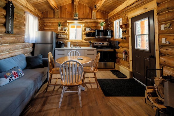 A log cabin interior with a kitchen, dining area, and a sofa with a decorative pillow.