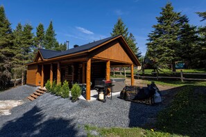 A log cabin with a porch, outdoor seating, and a grill.