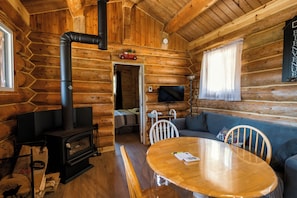 A log cabin interior with a fireplace, a television, a sofa, and a dining table.