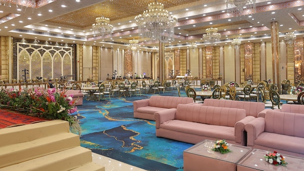 A spacious banquet hall with tiered seating, chandeliers, and a carpeted floor. - The Sandalwood By La Carnation (Sohna)