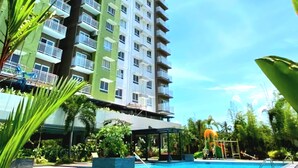 Un edificio alto con múltiples balcones y una zona de piscina rodeada de vegetación.