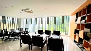 Una sala de reuniones moderna con una mesa grande y sillas, ventanas amplias con persianas verticales, y una estantería empotrada.