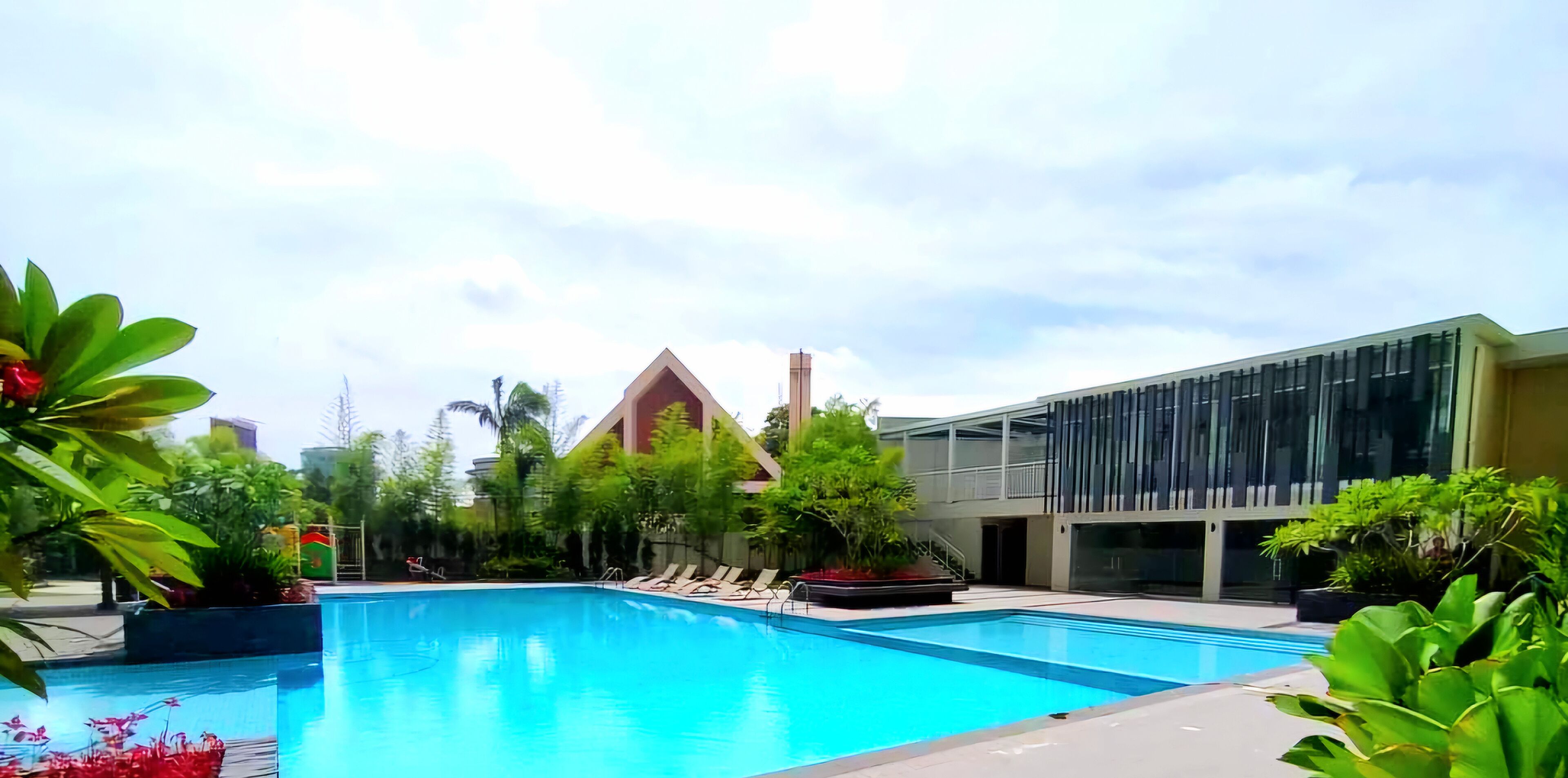 A swimming pool with lounge chairs, surrounded by greenery and modern buildings.