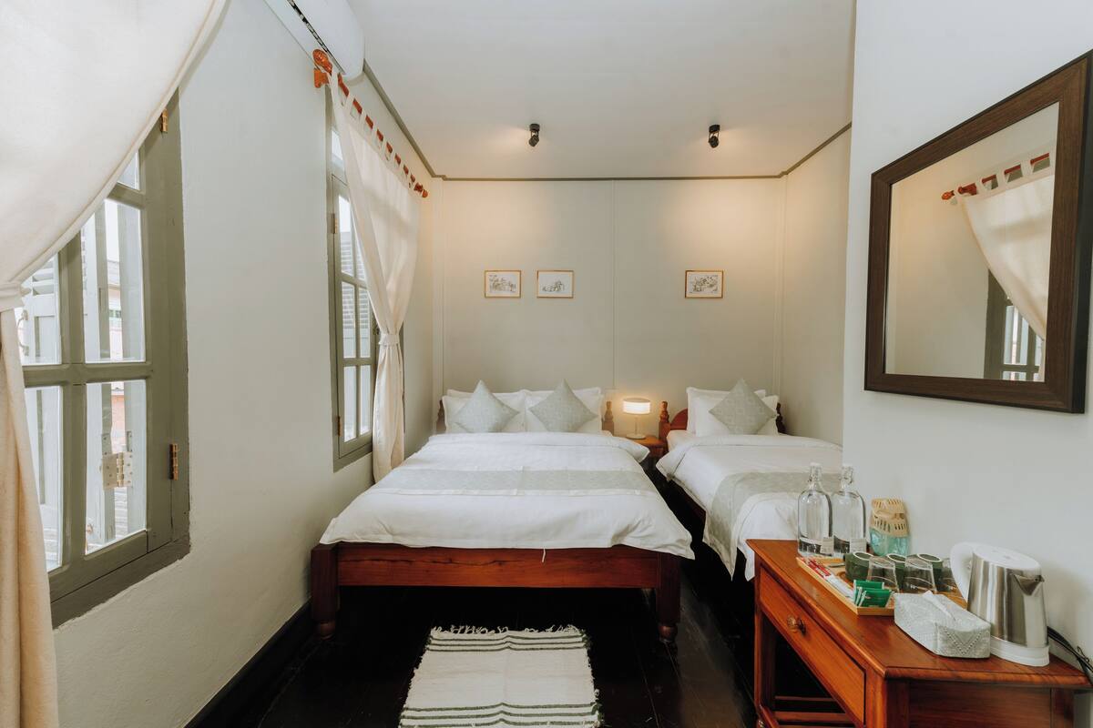Quarto com duas camas, uma mesa de cabeceira de madeira e um espelho.
