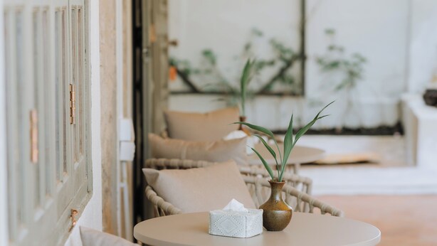 A row of wicker tables with cushions, a vase with a plant, and a tissue box on each table. - Samailaos Residence (Luang Prabang)