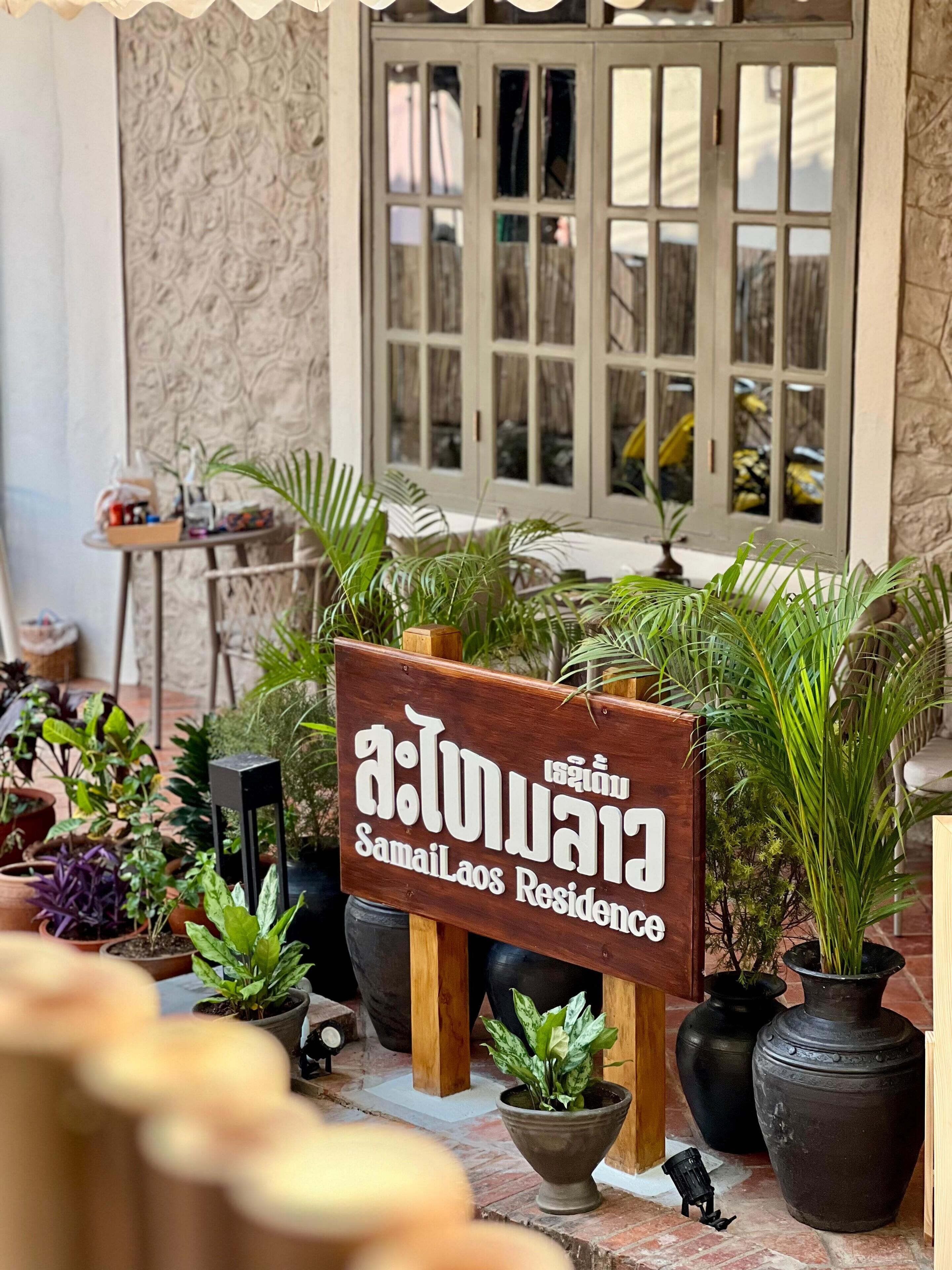 A signboard for Samail Laos Residence with potted plants around it.