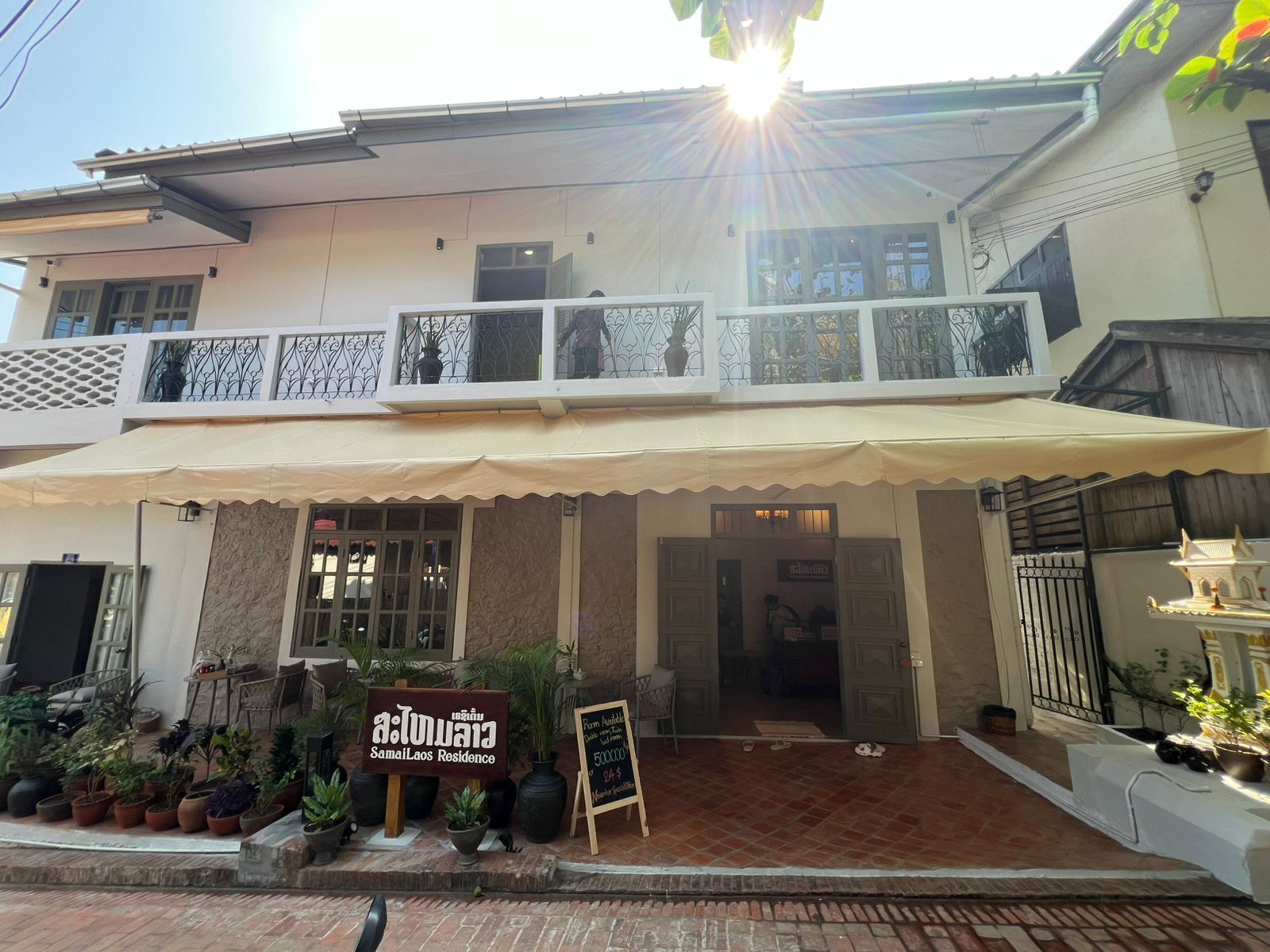 A two-story building with a balcony, a signboard, and potted plants.