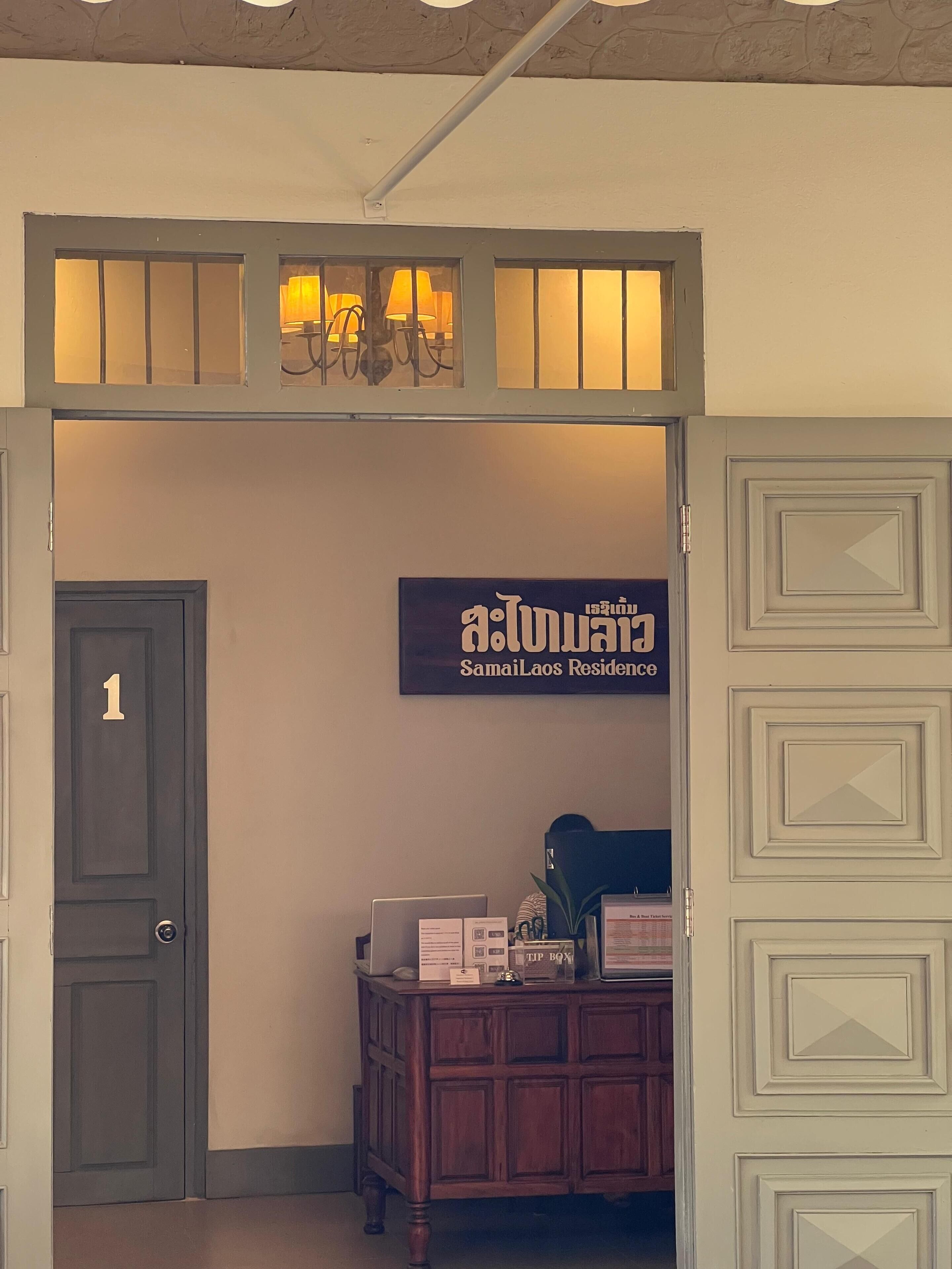 Une entrée d’immeuble avec une enseigne indiquant « Samai Laos Residence » et une porte portant le numéro « 1 ».