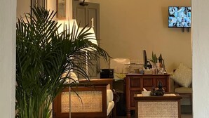 A cozy living room with a large potted plant, wicker furniture, a television, and a chandelier. - Samailaos Residence (Luang Prabang)