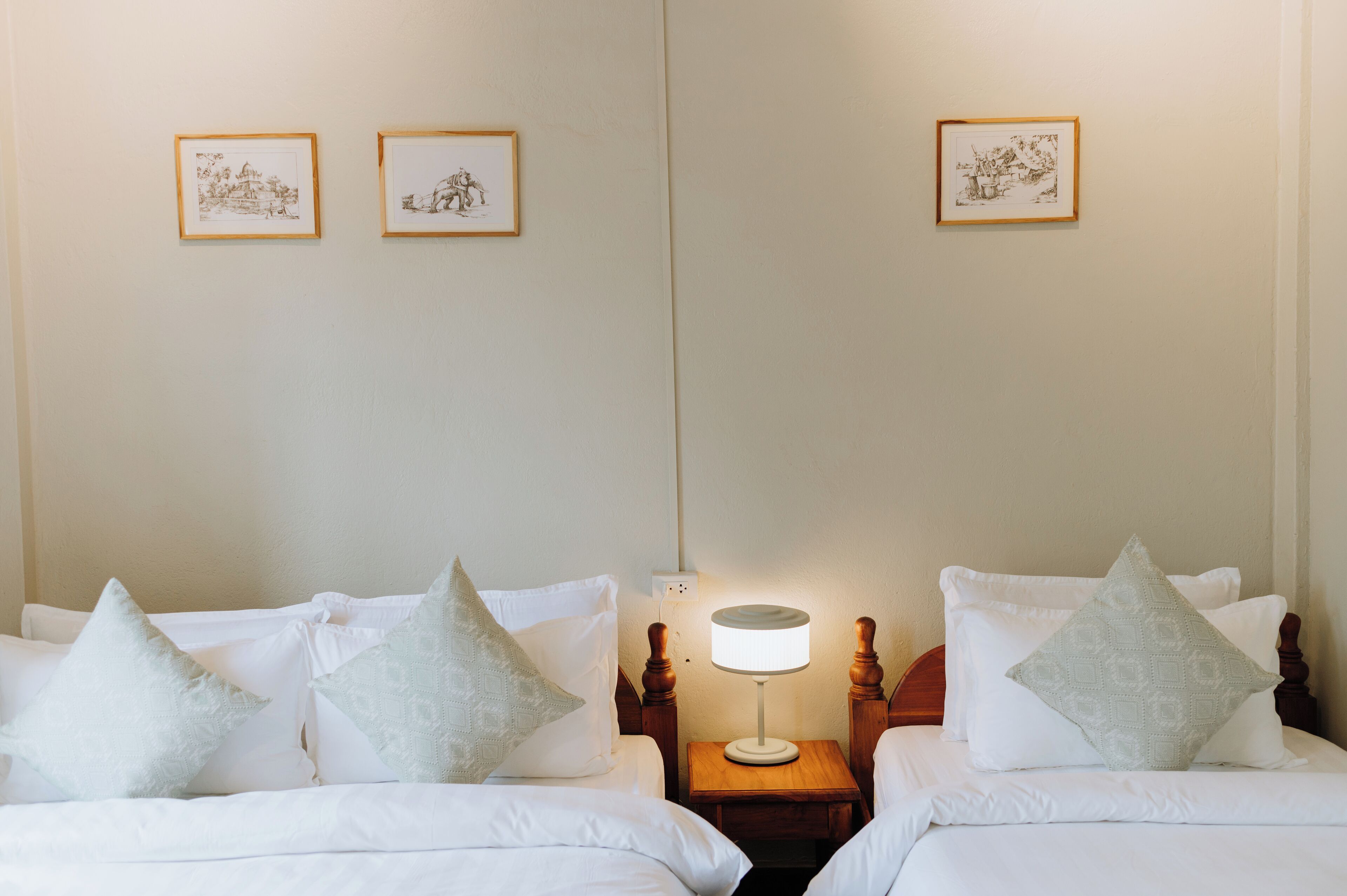 Une chambre d’hôtel avec deux lits, une table de chevet avec une lampe et deux tableaux encadrés au mur.