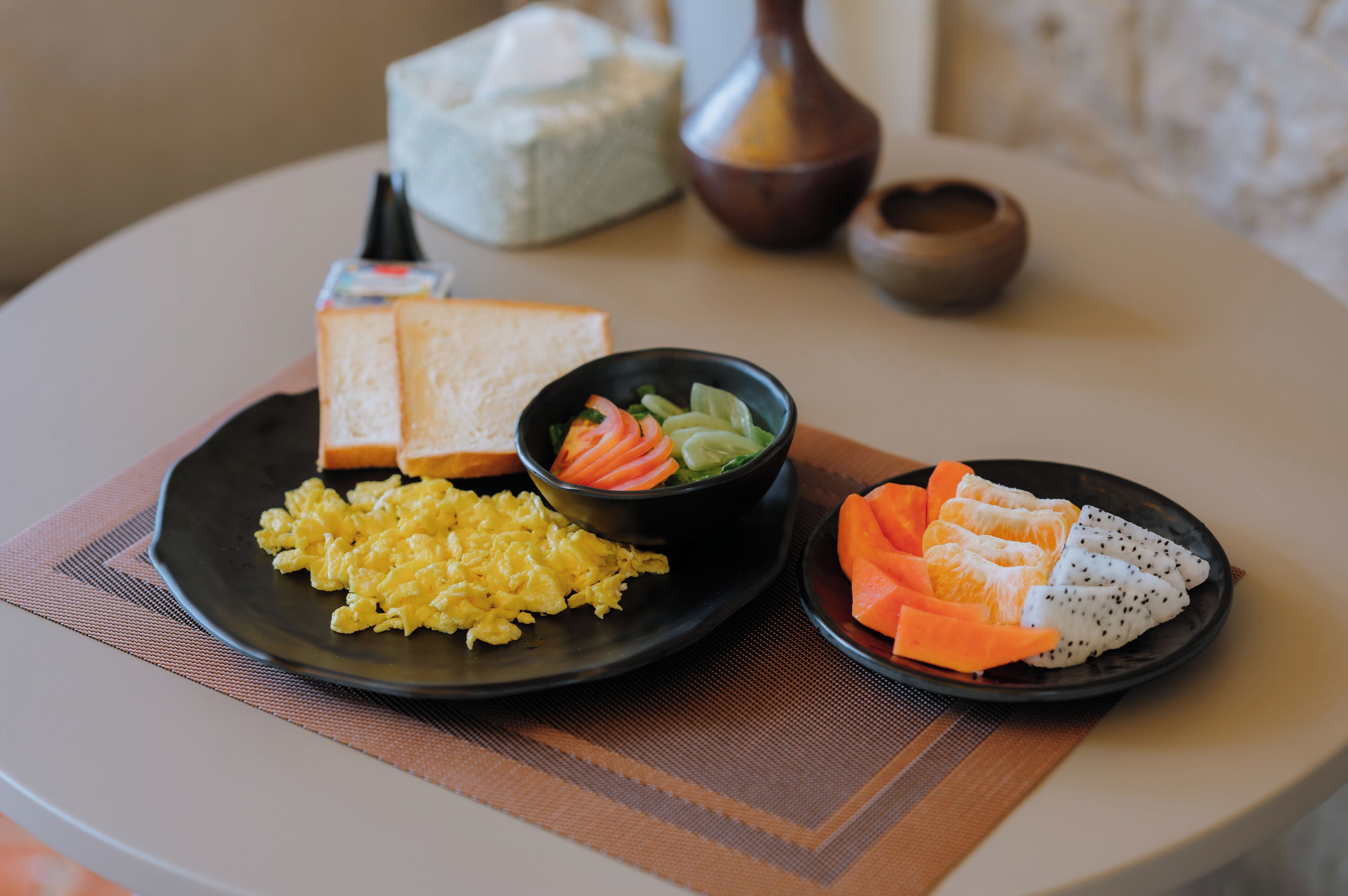 A table with plates of scrambled eggs, toast, and a bowl of salad.