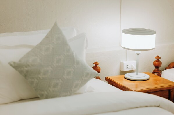 Una cama bien hecha, con una almohada blanca y una mesita de noche con una lámpara.