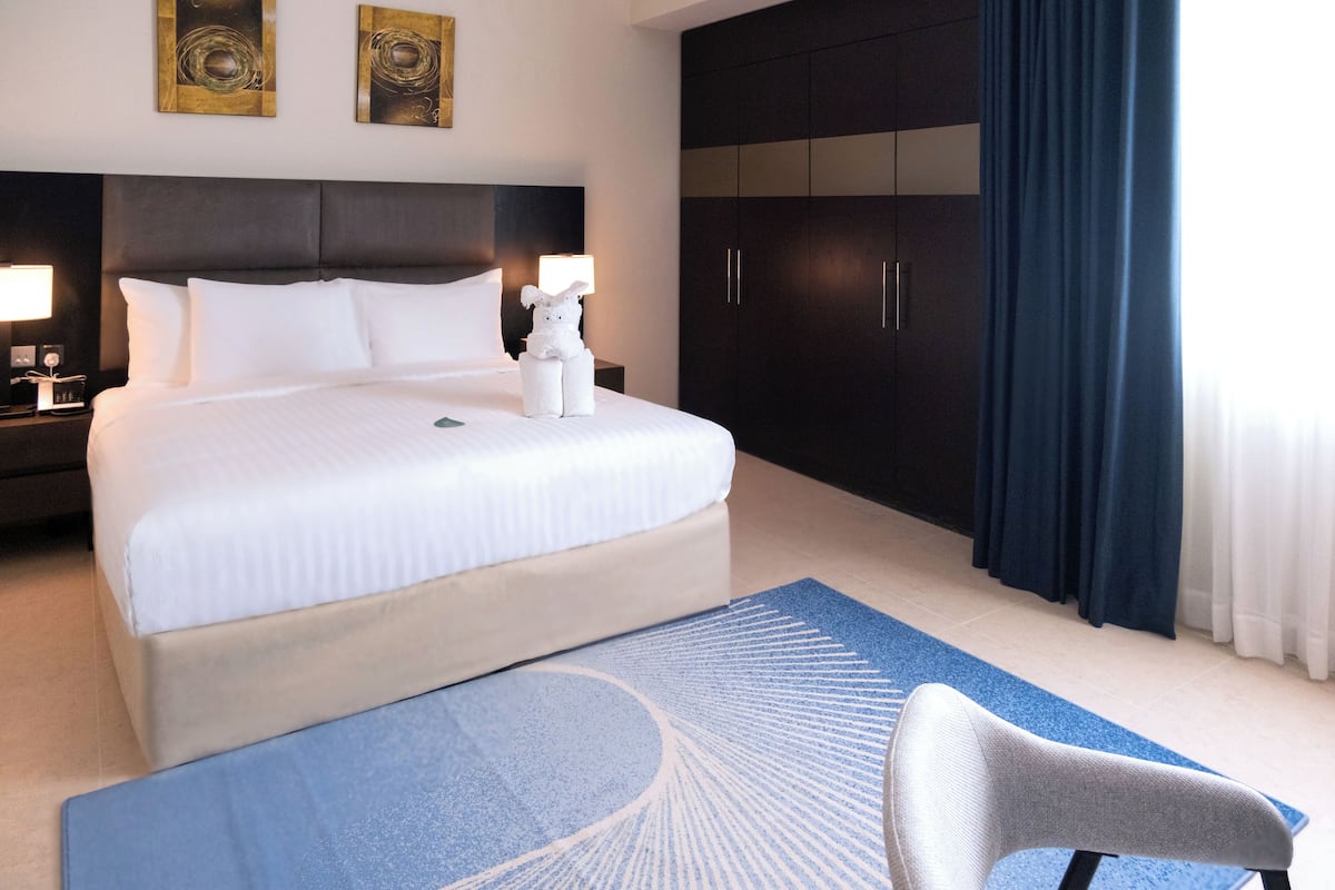 Een hotelkamer met een groot bed, een donkere houten garderobe en een blauw vloerkleed.