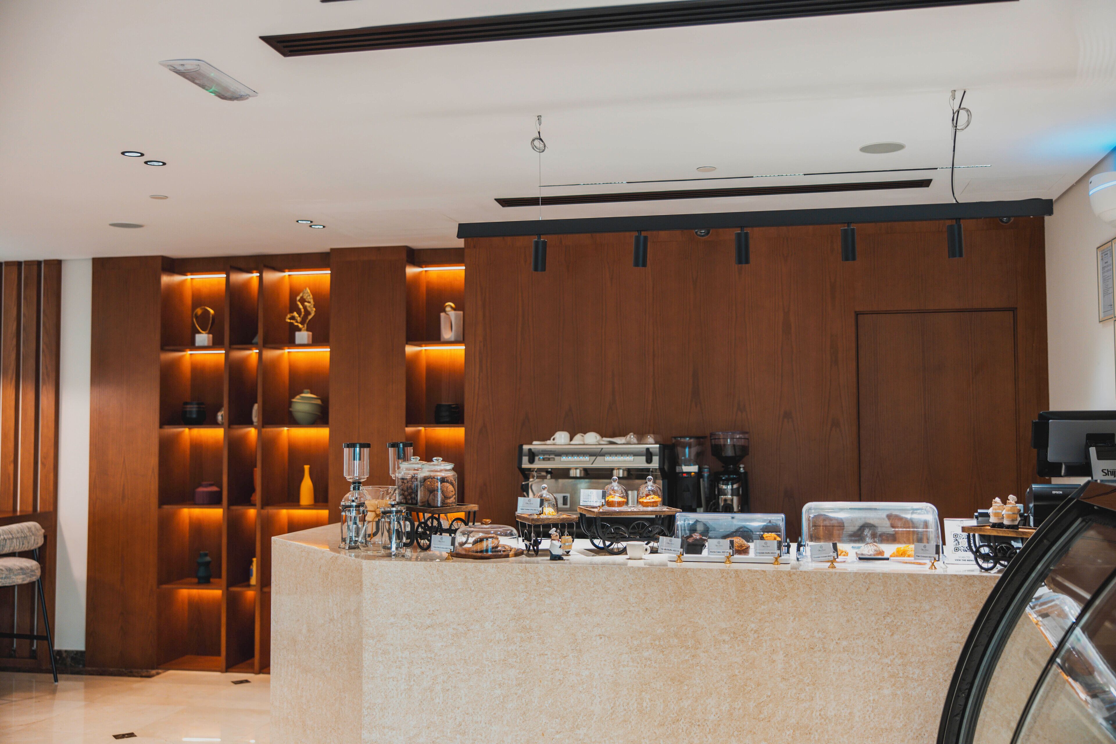 A modern hotel lobby with a reception desk, coffee machines, and a seating area.