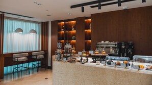 A modern hotel lobby with a coffee station, seating area, and a view of the cityscape. - Jannah Executive Hotel Apartments (Abu Dhabi)