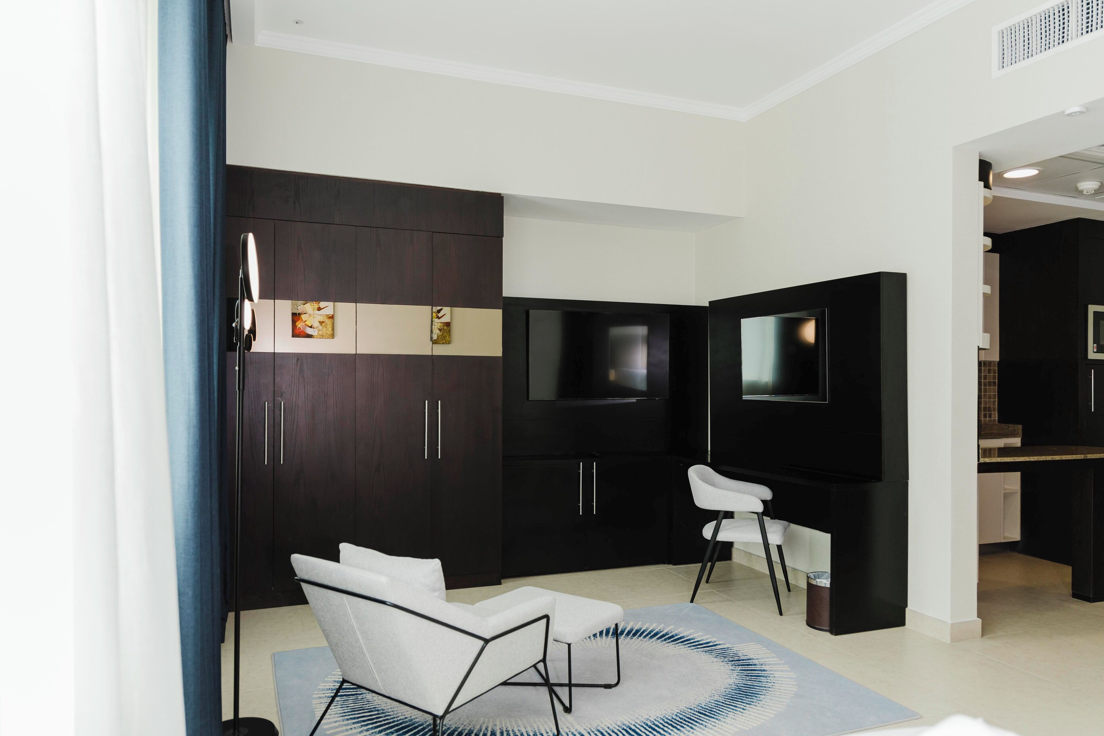 A modern living room with dark wood cabinets, a flat-screen TV, a white sofa, and a small kitchen area.