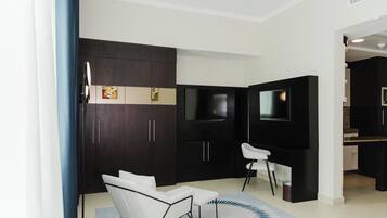 A modern living room with dark wood cabinets, a flat-screen TV, a white sofa, and a small kitchen area.