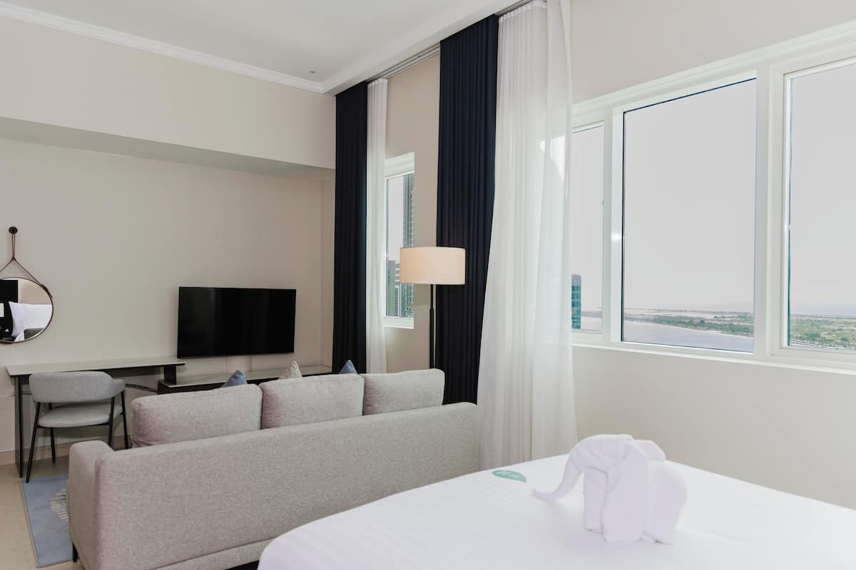Een hotelkamer met een bed, een slaapbank, een televisie, een bureau en een raam met uitzicht.