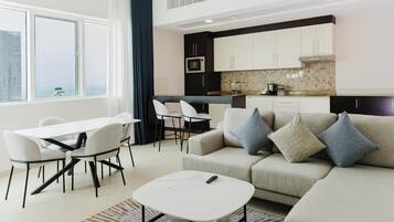 A modern living room with a sofa, a dining table, and chairs. There is a kitchen area with cabinets and a microwave.