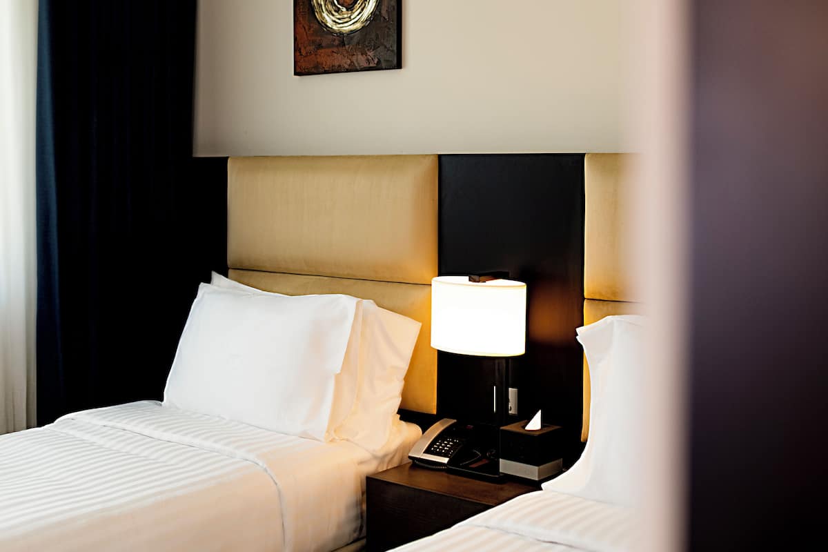 Een hotelkamer met twee bedden, een nachtkastje met een lamp, een telefoon en een kunstwerk aan de muur.