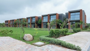 A modern building with multiple floors, large windows, and a well-maintained garden with various plants and a large rock.