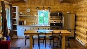A log cabin interior with a wooden dining table, chairs, a kitchen with appliances, and a window. - La Pitoune SPA privé - 6 pers  (Saint-Luc-de-Bellechasse)