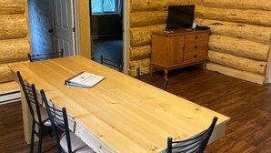 A wooden dining table with chairs, a television on a wooden cabinet, and a door leading to another room. - La Pitoune SPA privé - 6 pers  (Saint-Luc-de-Bellechasse)
