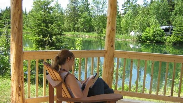 A wooden deck with a chair overlooking a lake, surrounded by trees. - La Pitoune SPA privé - 6 pers  (Saint-Luc-de-Bellechasse)