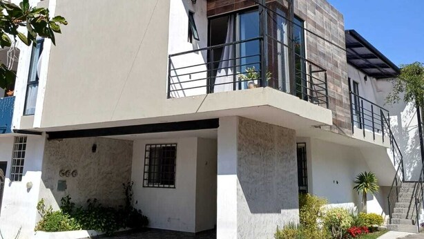 Una casa moderna de dos pisos con techo plano, ventanas grandes y un balcón.
