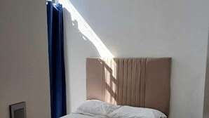 Un dormitorio con cama, cabecera, ventana con cortinas y puerta.