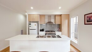 A modern kitchen with white cabinetry, a central island, a built-in stove, and a refrigerator. - Jubilee Home/Spacious Bedrooms/Comfy Beds/Smart TV (Manor Lakes)