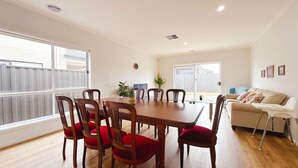 A dining area with a wooden table and red upholstered chairs, a sofa, and a television in the background. - Jubilee Home/Spacious Bedrooms/Comfy Beds/Smart TV (Manor Lakes)
