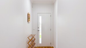 A hallway with a white door, a small shelf with a picture frame, and a wooden rack. - Jubilee Home/Spacious Bedrooms/Comfy Beds/Smart TV (Manor Lakes)