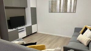 Un salon moderne avec un canapé gris, un téléviseur à écran plat posé sur un meuble de télévision blanc et une œuvre d’art minimaliste accrochée au mur.