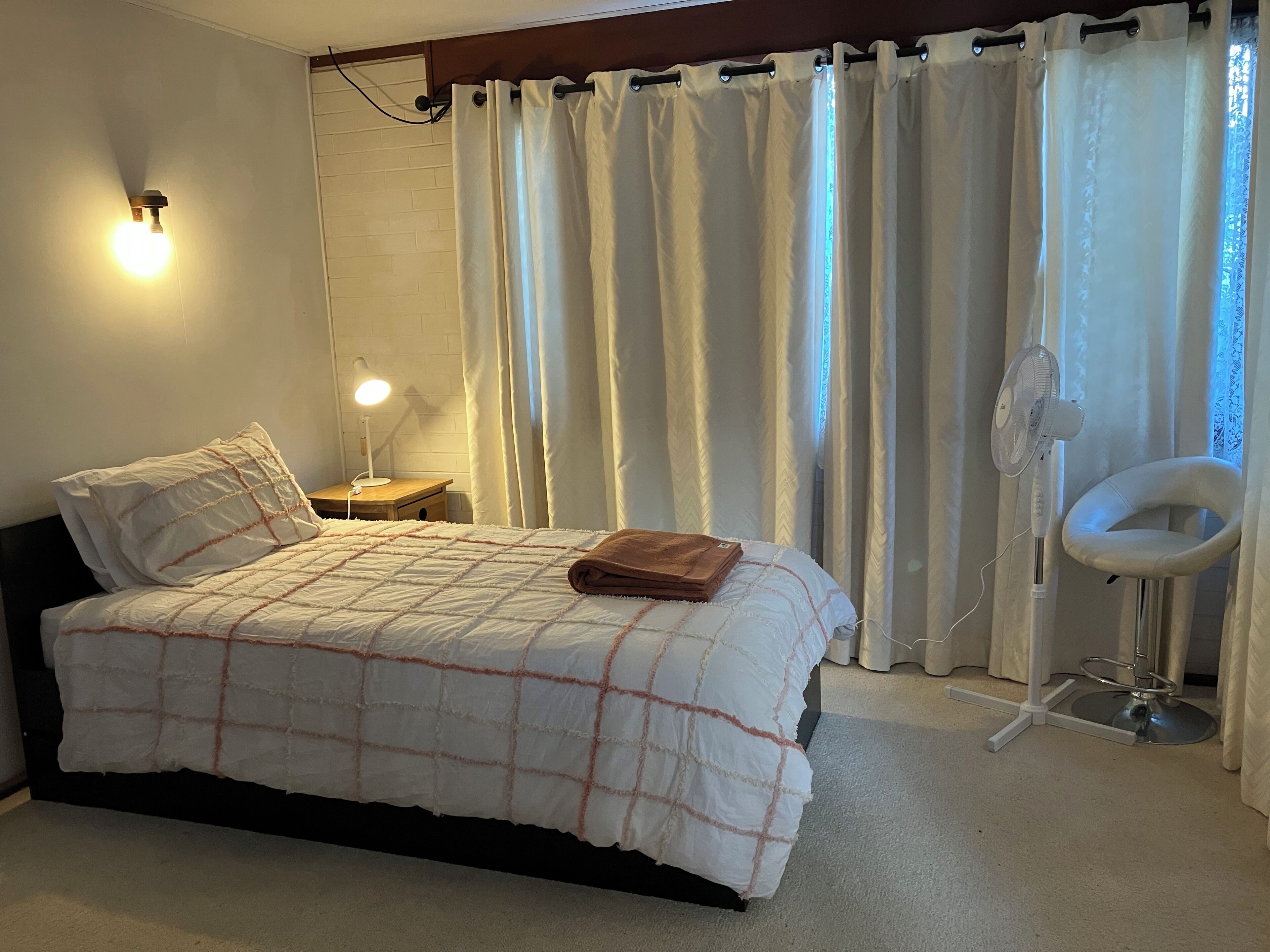 Une chambre à coucher avec un lit, une lampe de chevet, un ventilateur et une chaise.