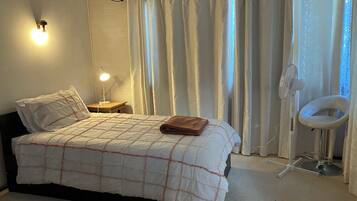 Une chambre à coucher avec un lit, une lampe de chevet, un ventilateur et une chaise.
