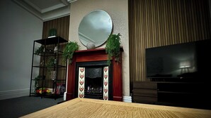 A room with a fireplace, a television, and a wooden table. - Sleeps10-parking-garden-hottub-petfriendly (Blackpool)