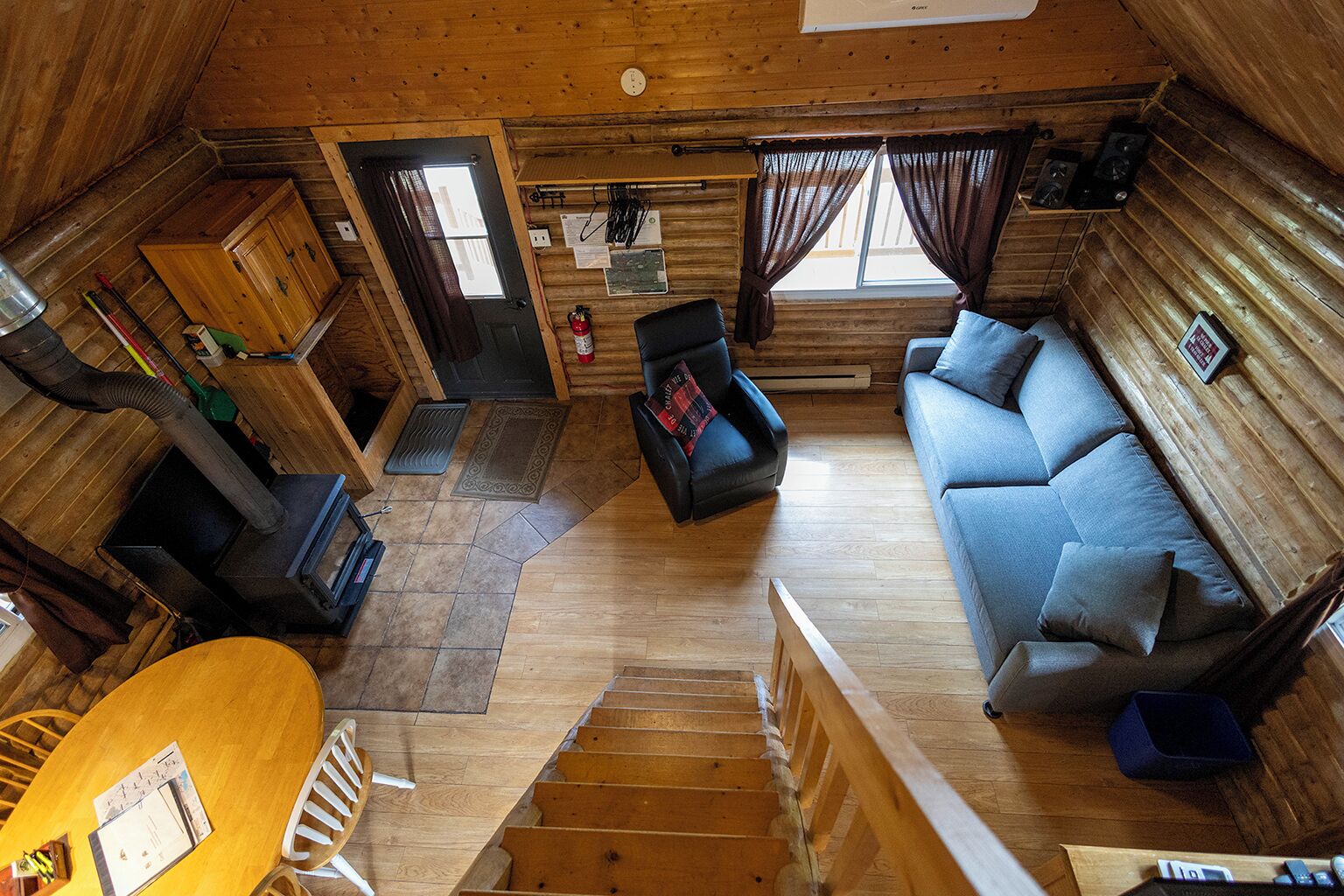 Un interior de cabaña con piso de madera, un sofá, una mesa de comedor y una escalera.