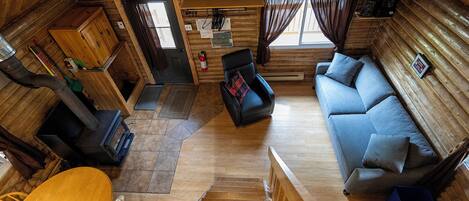 Un interior de cabaña con piso de madera, un sofá, una mesa de comedor y una escalera.
