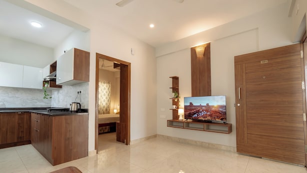 A modern kitchen with wooden cabinets, a marble countertop, and a built-in TV.