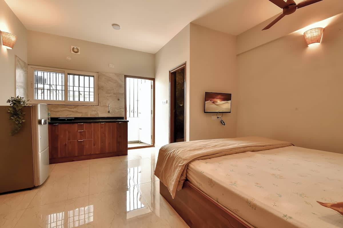 Een moderne slaapkamer met een groot bed, een houten dressoir, een ingebouwde keuken met raam en een plafondventilator.