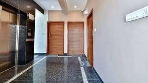 A modern hallway with a marble floor, two wooden doors, and an elevator.