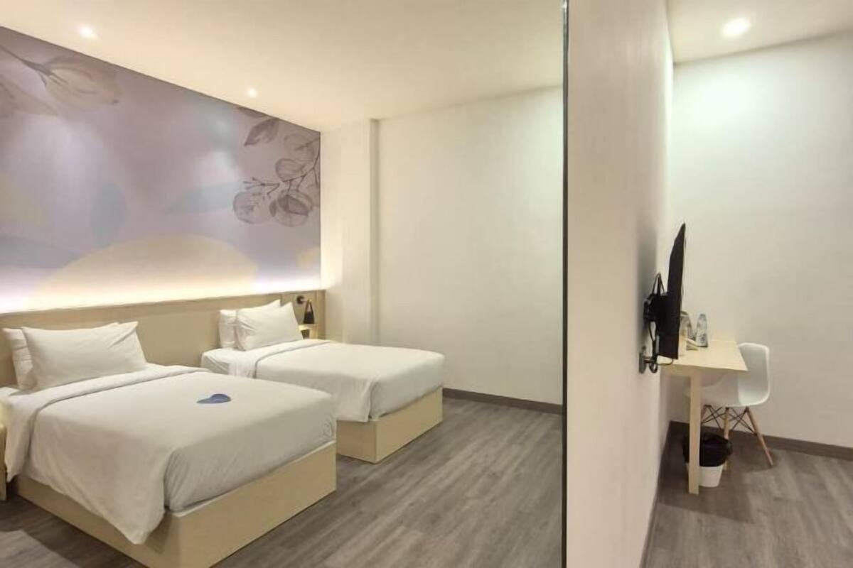 Una habitaci ón de hotel con dos camas, un escritorio, una silla y un televisor instalado en la pared.