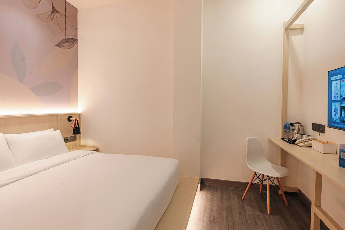 Habitación de hotel con cama, escritorio, silla, computadora y pared decorada con motivos florales.