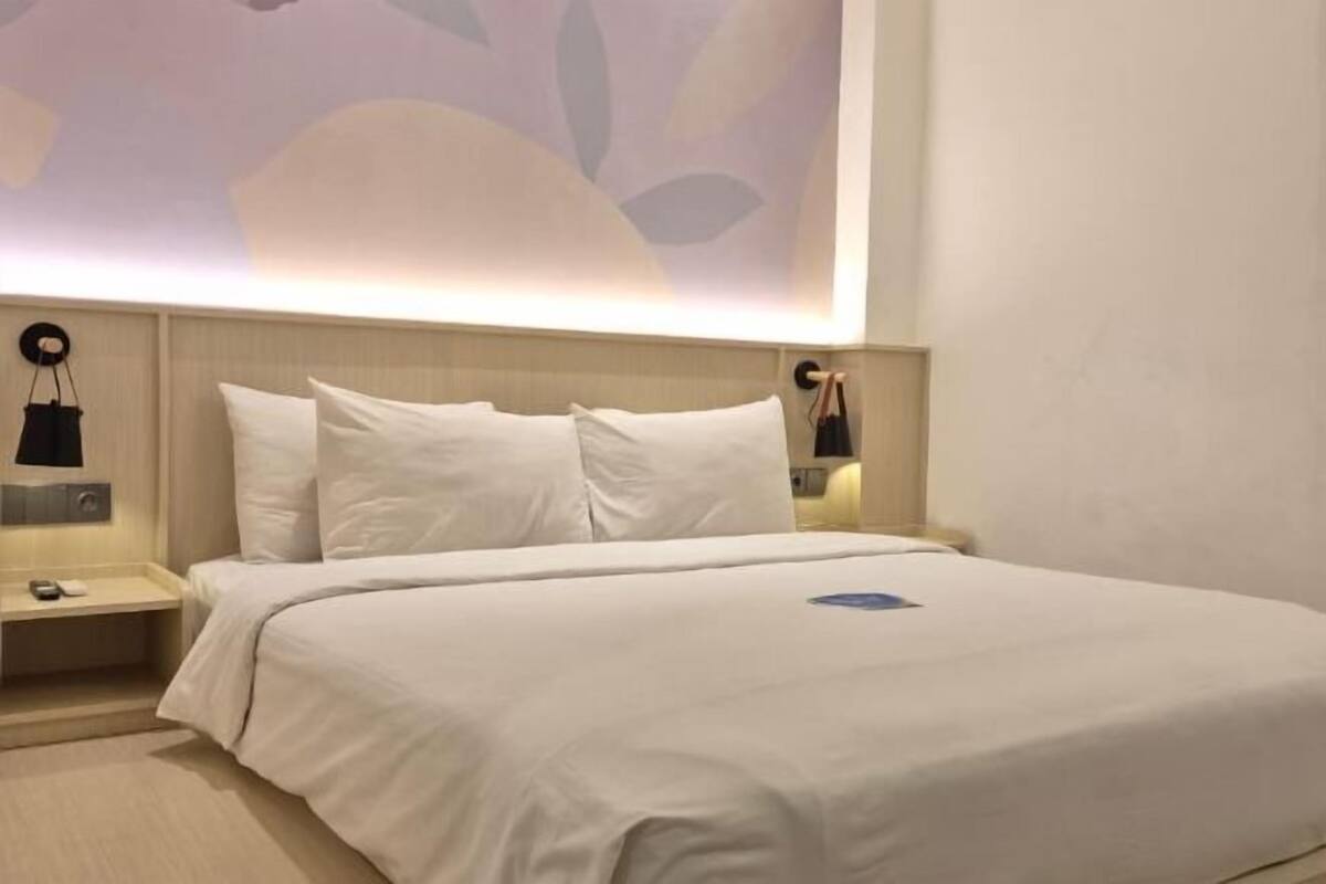Una habitación de hotel con una cama grande, cabecera, mesitas de noche y lámparas fijadas a la pared.