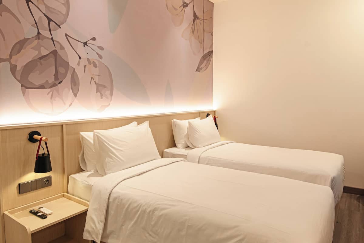 Una habitación de hotel moderna con dos camas, una mesita de noche con lámpara y una obra de arte colgada en la pared.
