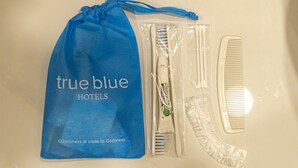 Eine blaue Tasche mit Kordelzug, beschriftet mit 'true blue hotels', mit Zahnbürste, Kamm und Rasierer in Plastikverpackung.